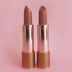 Two nude lipsticks with gold caps on a pink background