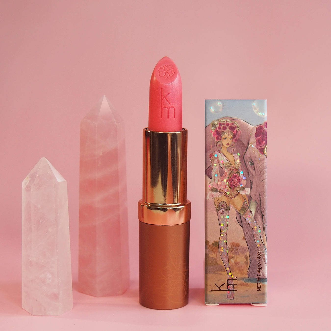 Pink lipstick with gold cap and decorative packaging on a pink background