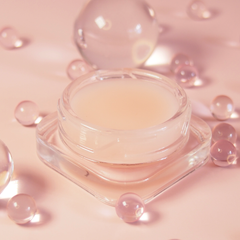 Cosmetic jar with a pinkish cream on a soft pink background with peptides. Anytime Lip Mask is a miracle lip treatment that delivers intense results in a soft pink package with a delicate lychee flavour. Vegan.