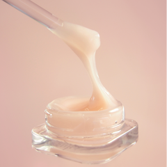 Glass jar of cream with a dropper on a pink background. 