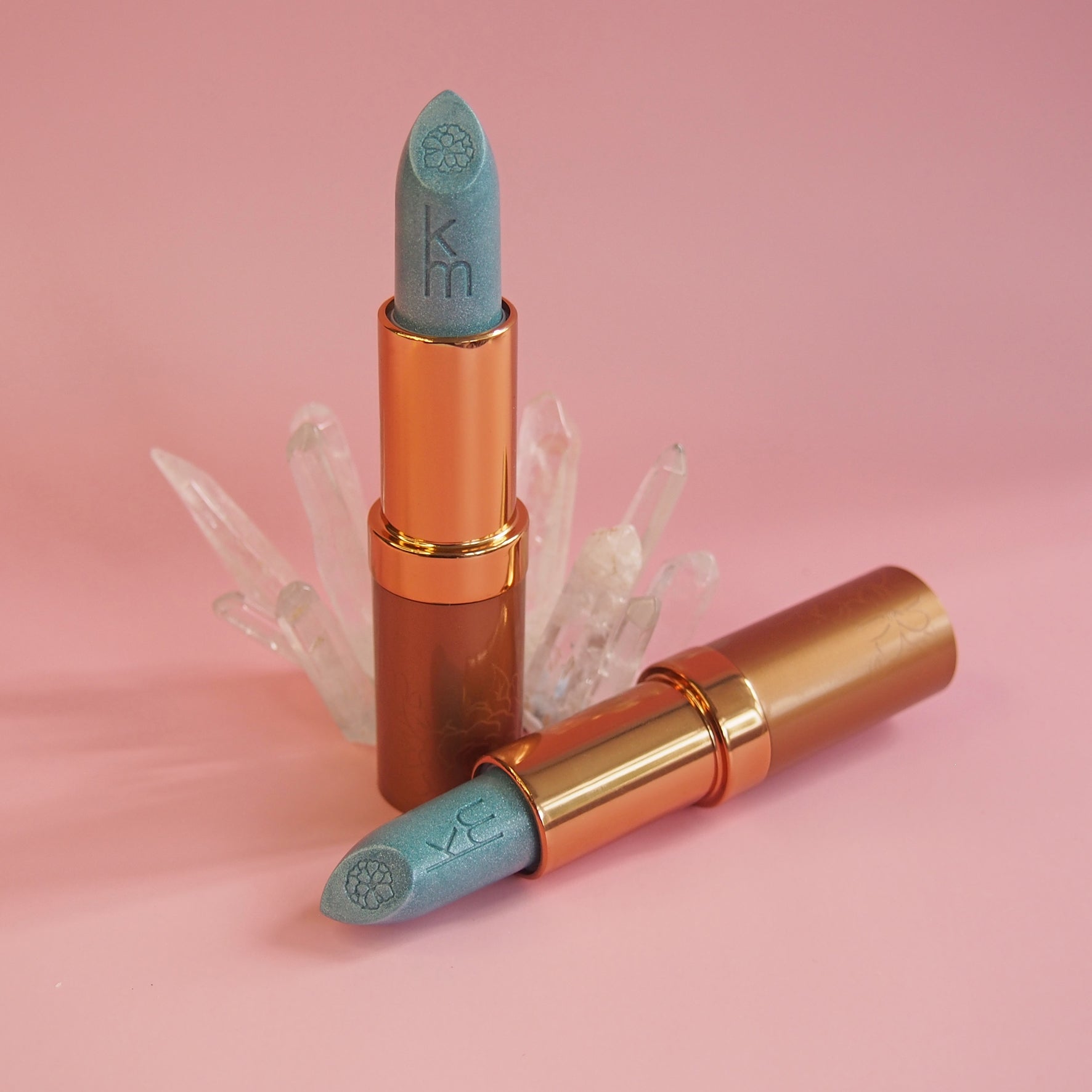Two lipsticks with blue caps and gold bodies on a pink background